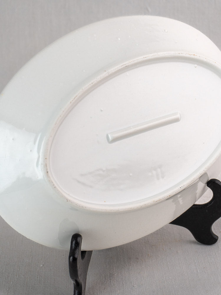 Antique French white ironstone oval platters, upside down on a black stand, unglazed bases visible.
