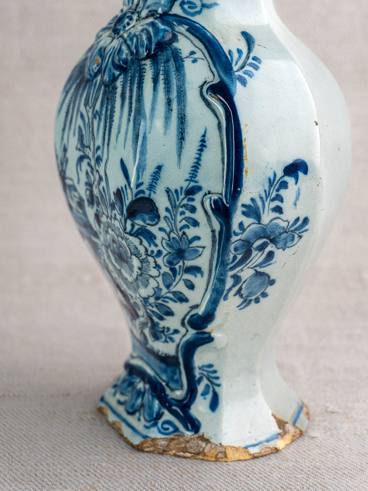 Antique Dutch Delft vase pair, c. 1700, with blue and white floral motifs, chipped base, on neutral fabric backdrop.