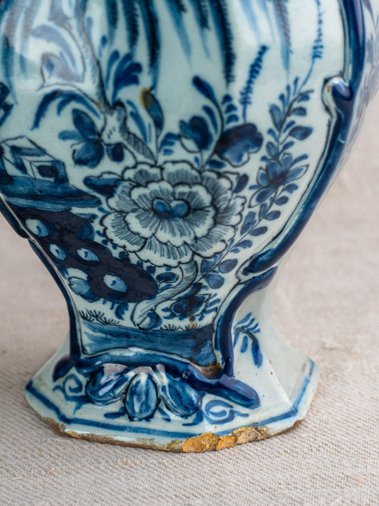 Antique Dutch Delft vase, c.1700, blue and white floral motifs with a house; worn base on beige textured surface.