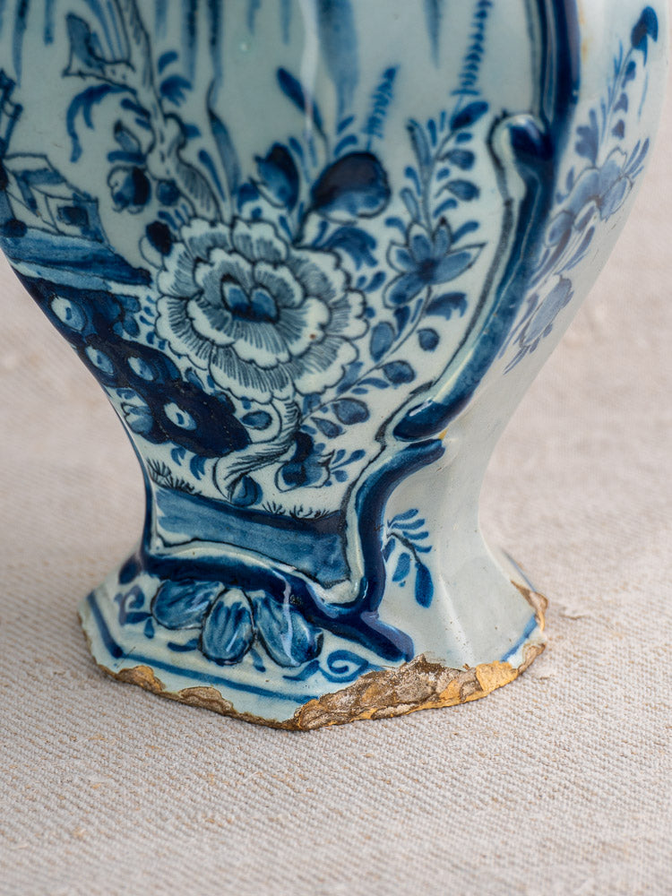 Close-up of antique Dutch Delft vase base with blue floral patterns, showing chips and cracks exposing worn material.