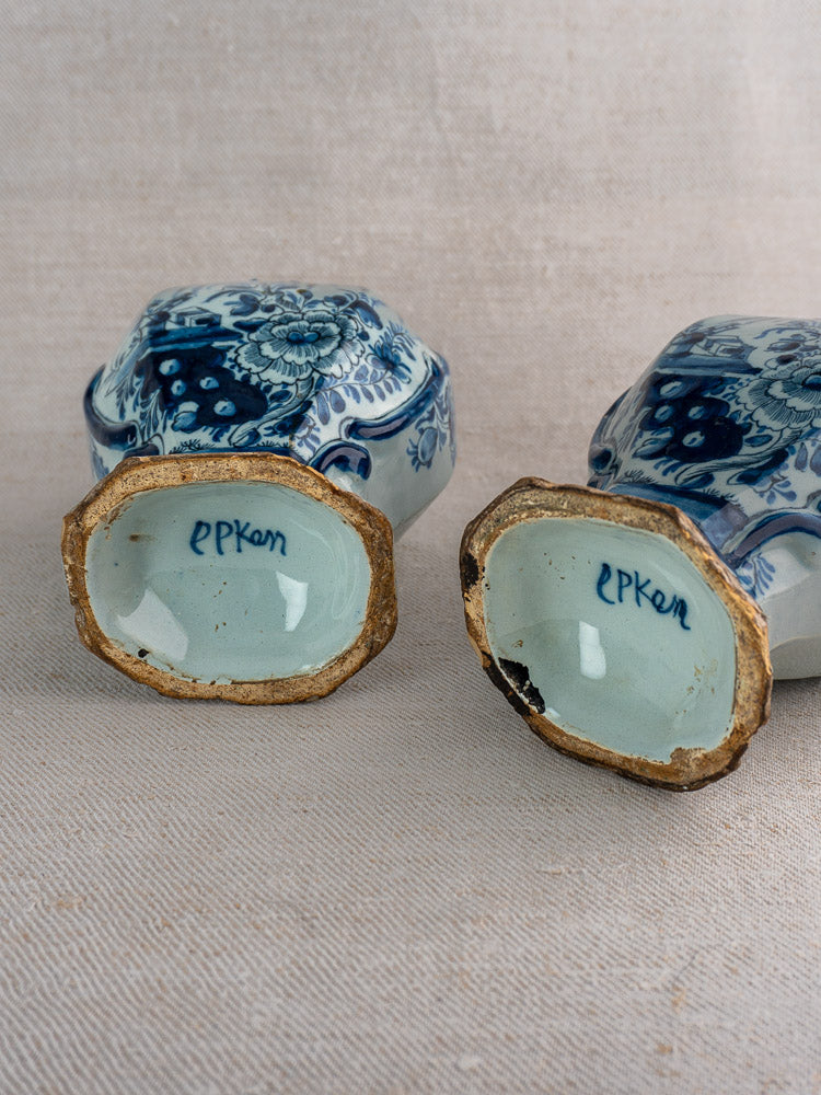 Pair of antique Dutch Delft blue and white vases upside down, showing floral designs and EPKam marks on neutral fabric.