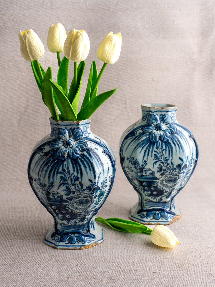 Antique Dutch Delft blue and white vases, circa 1700, each arranged with cream tulips, one blossom nearby.