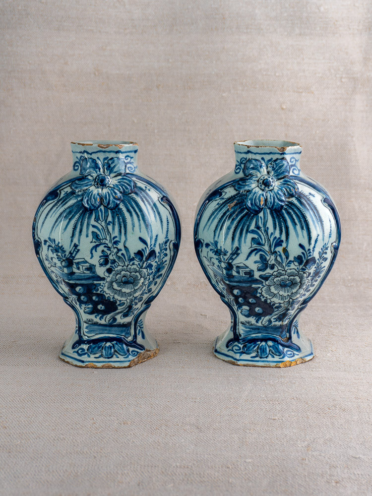 Pair of antique Dutch Delft blue and white vases with floral motifs and narrow necks on neutral fabric.