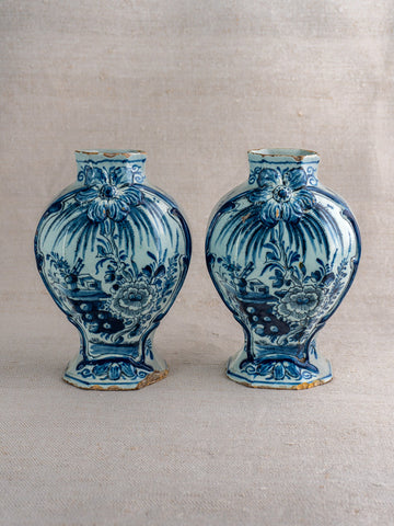 Pair of antique Dutch Delft blue and white vases with floral motifs and narrow necks on neutral fabric.