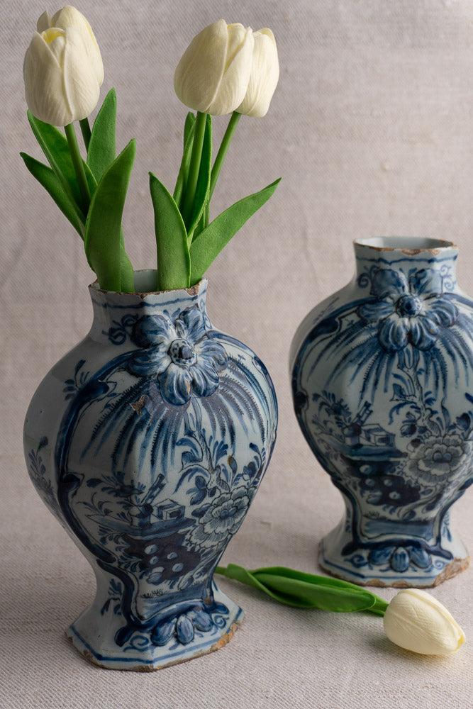 Antique blue and white Dutch Delft vase pair, one with three white tulips, on beige fabric.