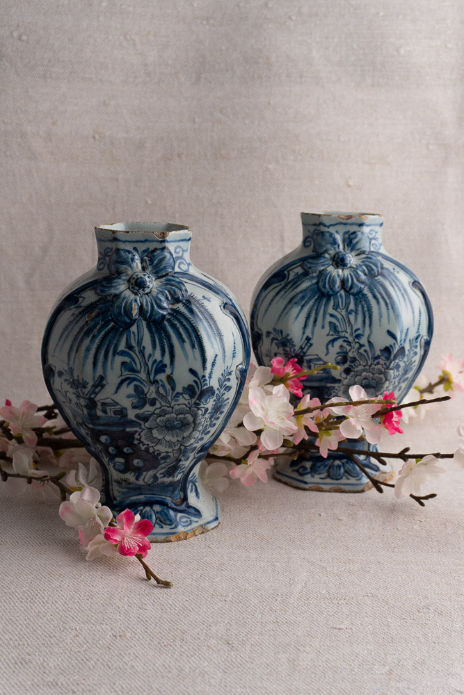 Antique Dutch Delft blue and white vase pair, c. 1700, with classic motifs and pink blossoms in front.
