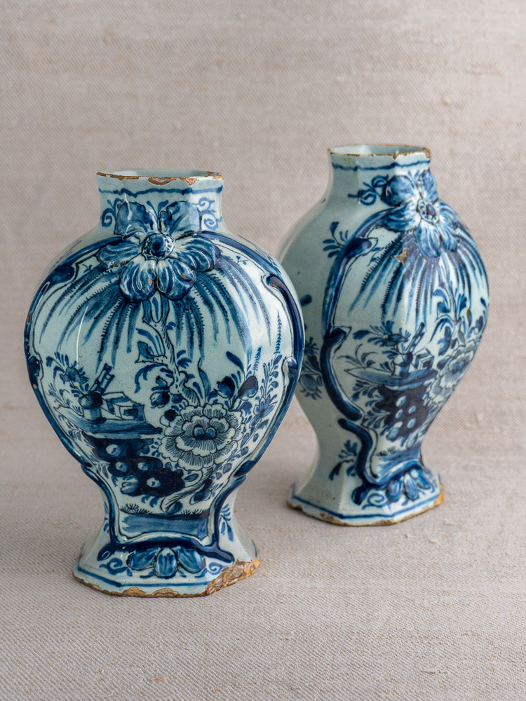 Antique Dutch Delft blue and white vases, circa 1700, floral scenic motifs, rim and base wear, on neutral fabric background.