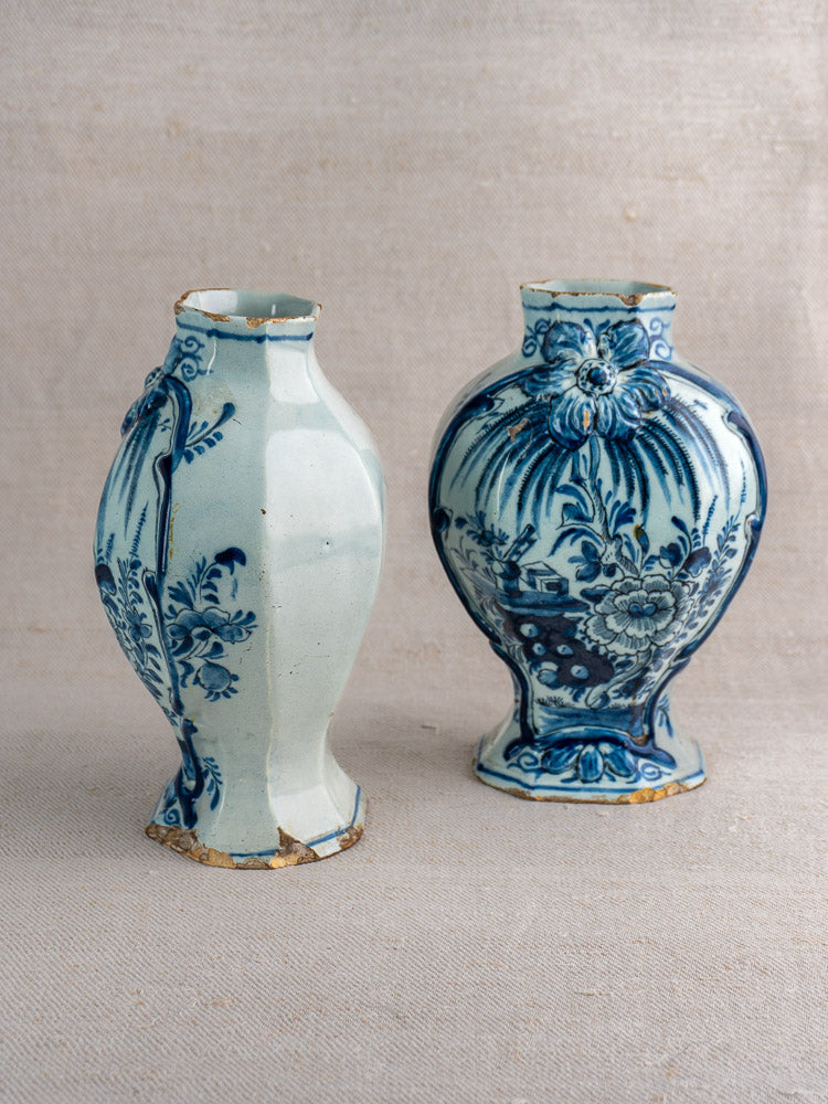 Pair of antique Dutch Delft vases, blue and white with floral and landscape designs, worn bases, on neutral fabric.