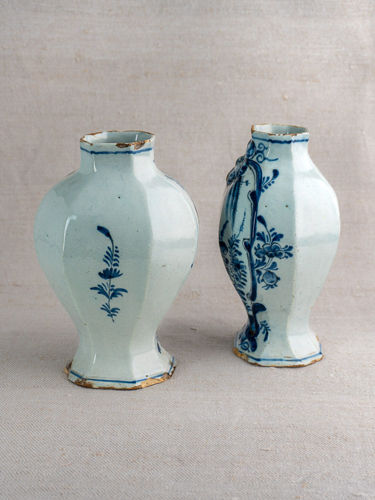 Pair of antique Dutch Delft vases with blue floral motifs and chipped rims on a neutral fabric backdrop.