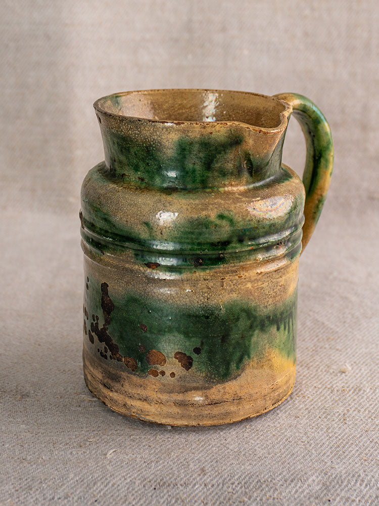 Pair of antique French Jaspé pitchers from Dieulefit with green glaze, wide mouths, on neutral textured fabric background.