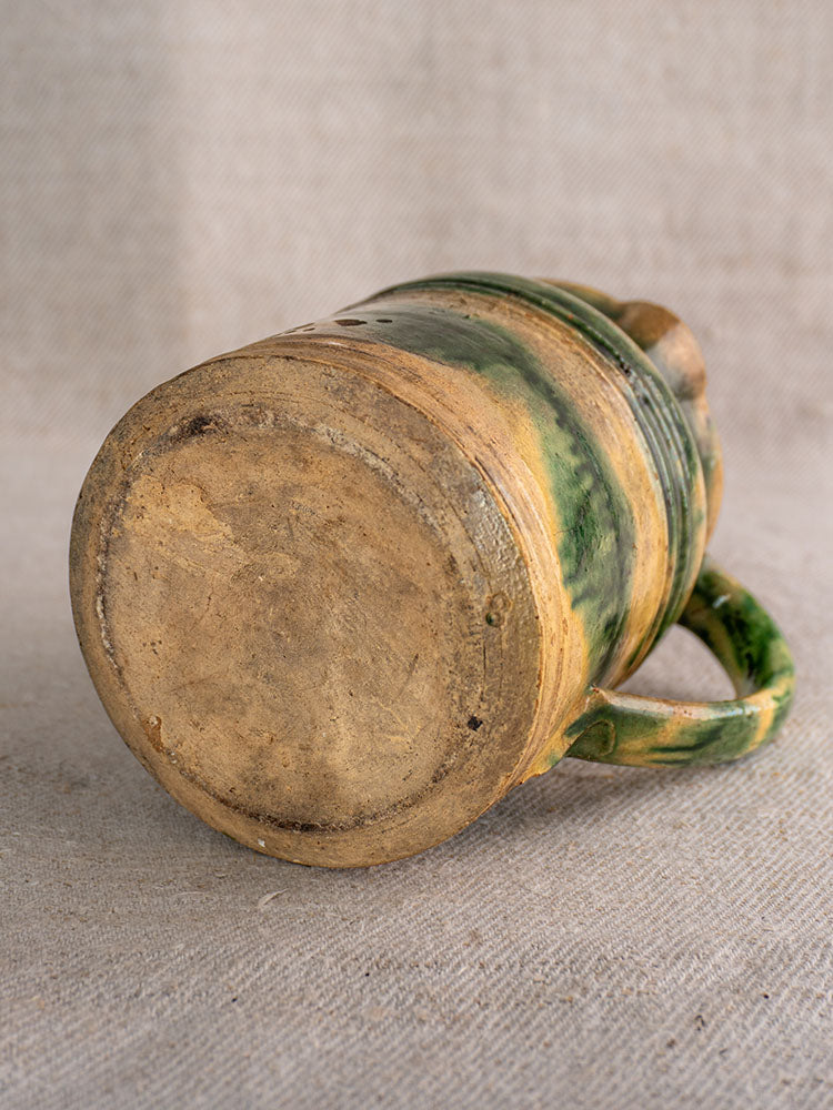 Pair of antique French Jaspé pitchers with green glaze from Dieulefit, showing textured base on woven fabric.