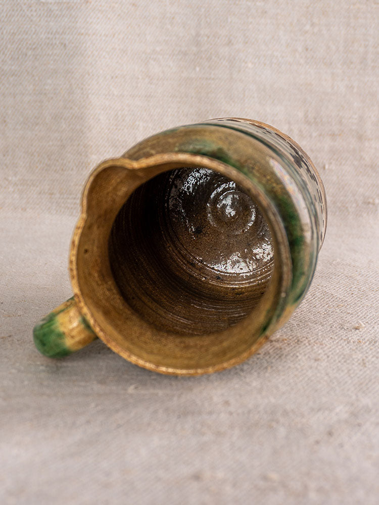 Pair of antique French jaspé pitchers with green glaze from Dieulefit on textured beige fabric background.