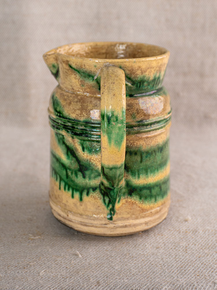 Pair of antique French Jaspé pitchers with green glaze and handles on textured beige fabric background.