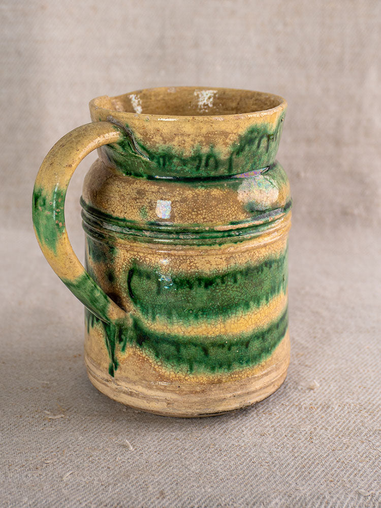 Pair of antique French Jaspé pitchers with green glaze from Dieulefit on textured beige fabric background.