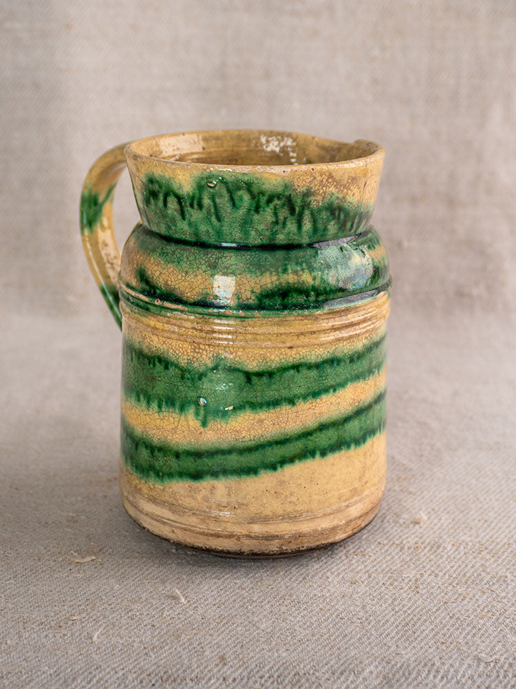 Pair of antique French Jaspé pitchers from Dieulefit with green glaze on a textured beige fabric background.