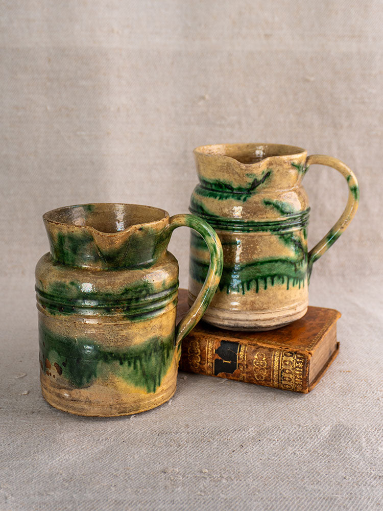 Pair of antique French Jaspé pitchers with green glaze from Dieulefit, one displayed on an ornate vintage book.