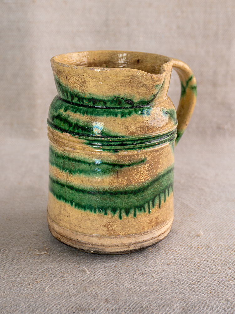 Pair of antique French Jaspé pitchers with green glazed stripes on tan clay, Dieulefit style, on beige textured fabric.