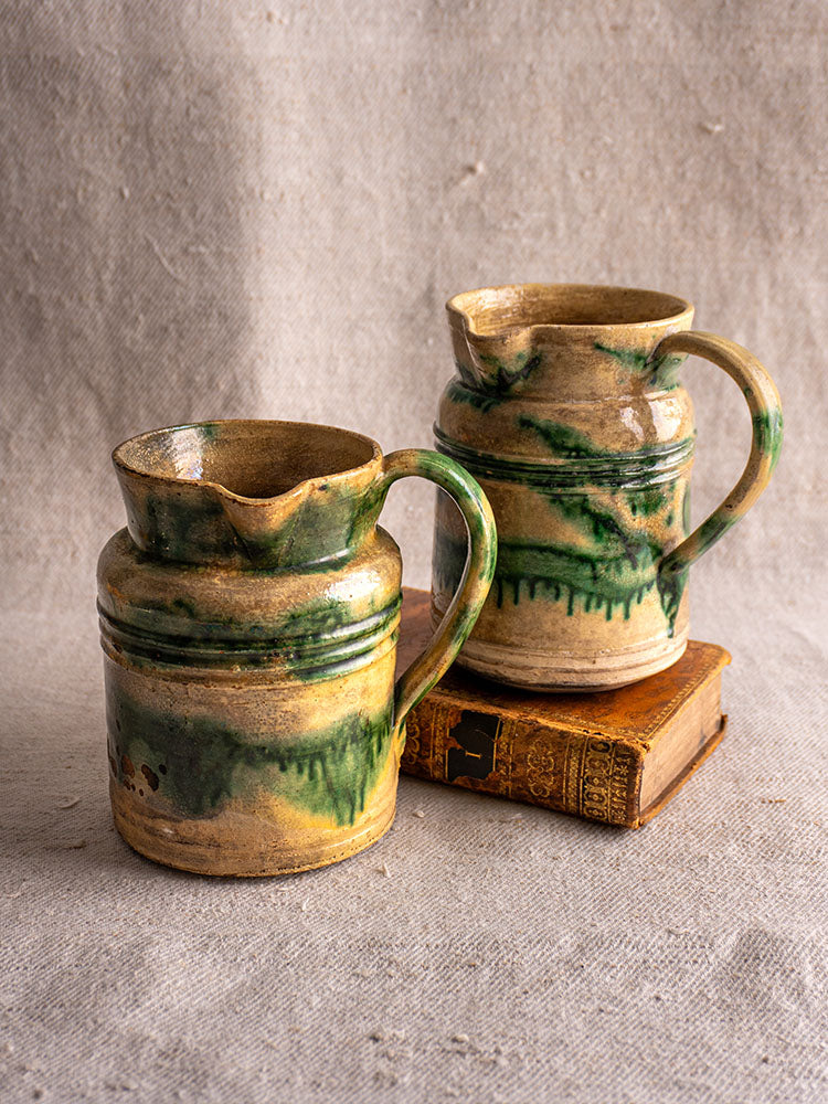 Antique French Jaspé pitchers with green glaze from Dieulefit on fabric, one atop vintage books, classic Drôme pottery style.