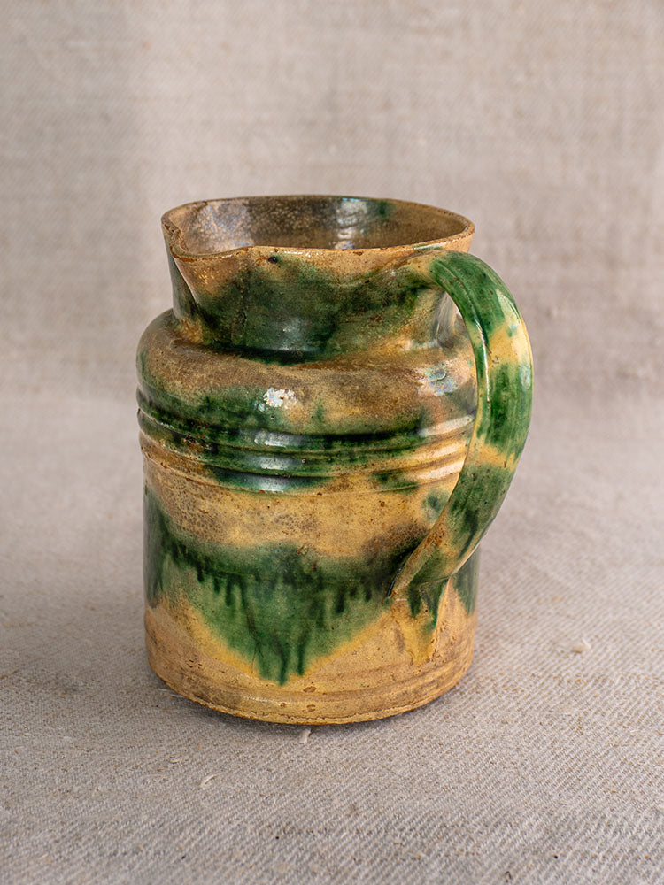 Pair of antique French Jaspé pitchers with green glaze from Dieulefit on a textured beige fabric background.