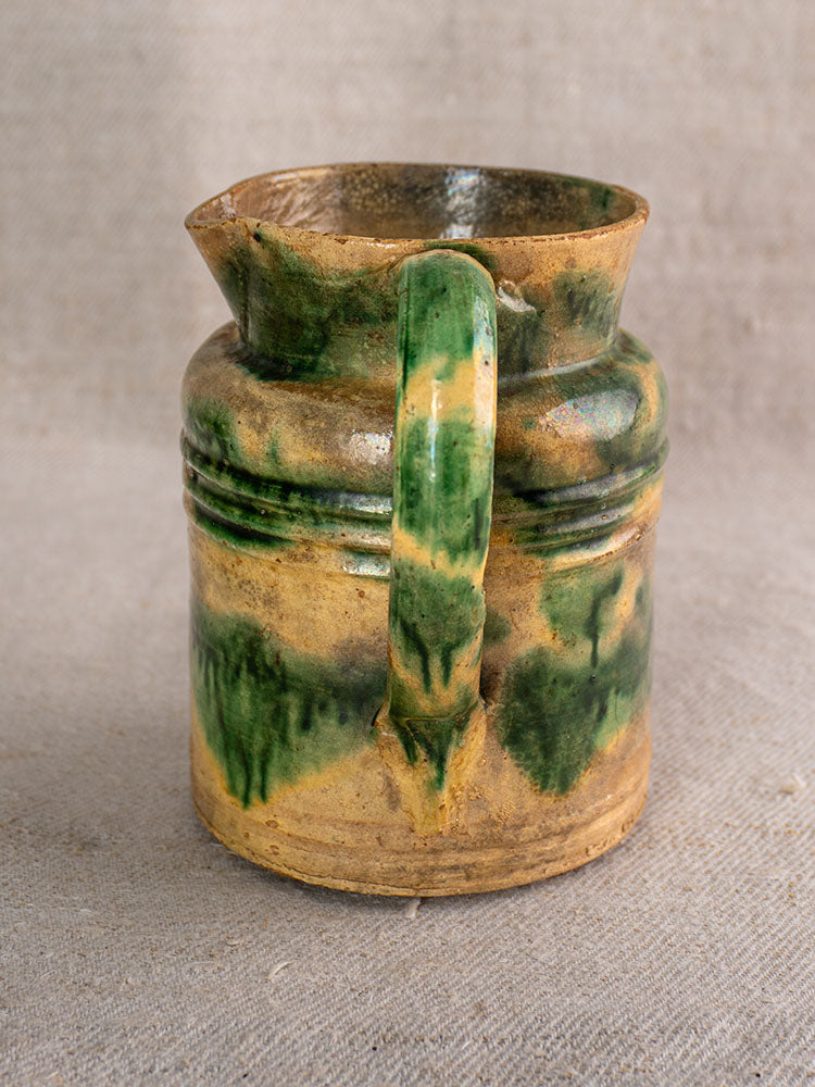 Pair of antique French Jaspé Dieulefit pitchers with green glaze over brown base on neutral textured fabric.