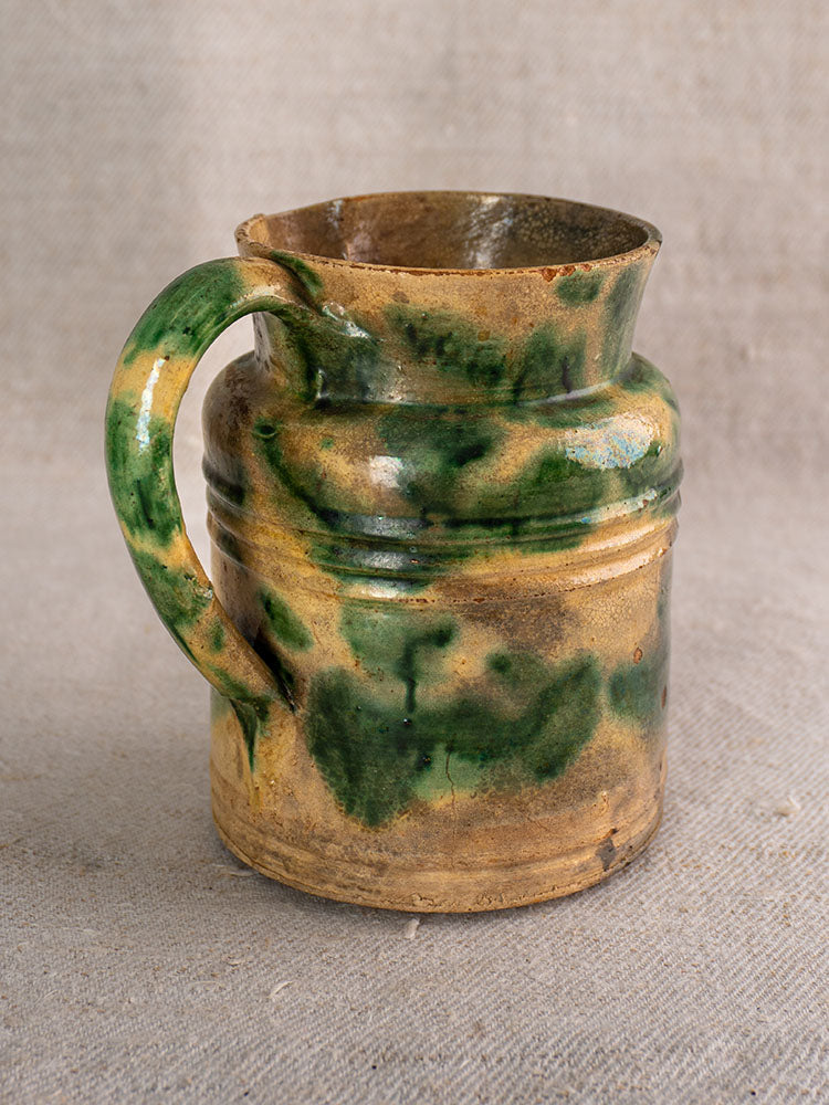 Antique French Jaspé pitchers with green glaze from Dieulefit on a textured beige fabric background.