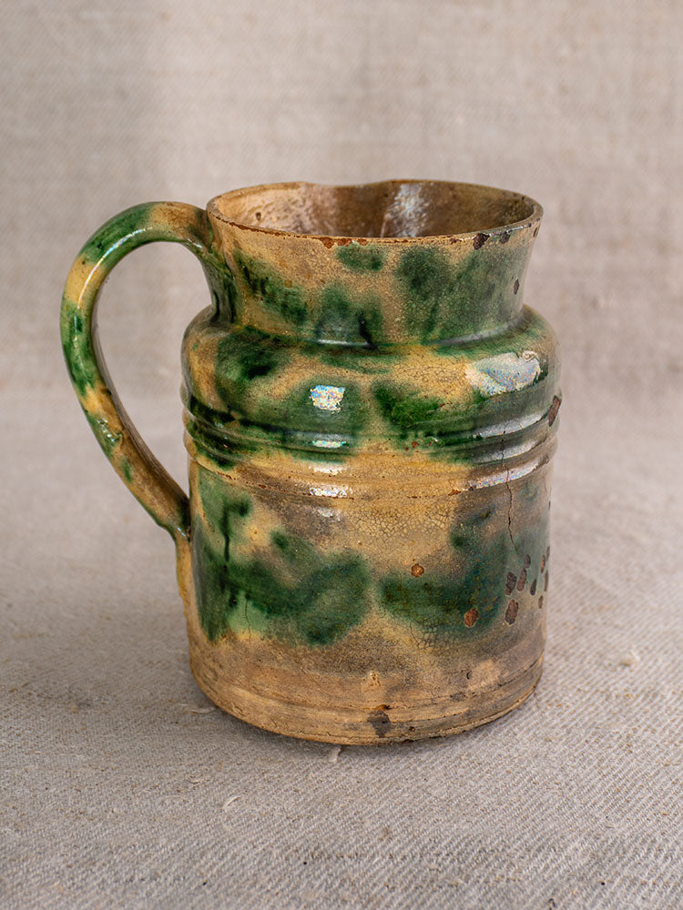 Pair of antique French Jaspé pitchers with green glaze and ridged tops on a textured beige fabric background.
