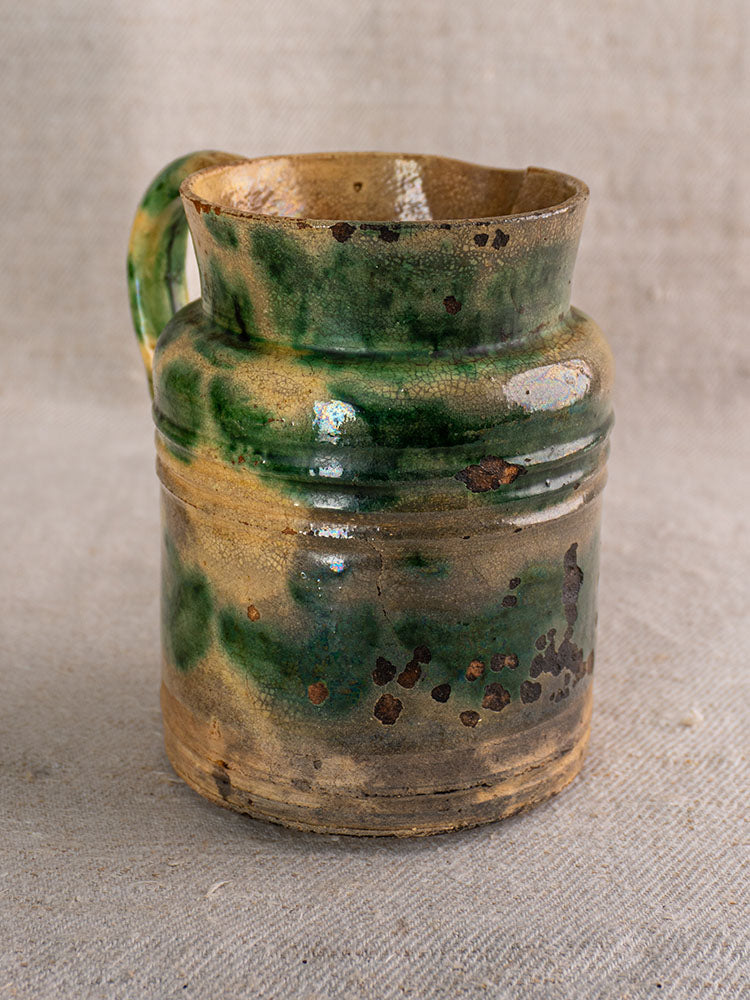 Antique French Jaspé pitchers from Dieulefit with green glaze, visible wear, and chips on beige textured fabric.