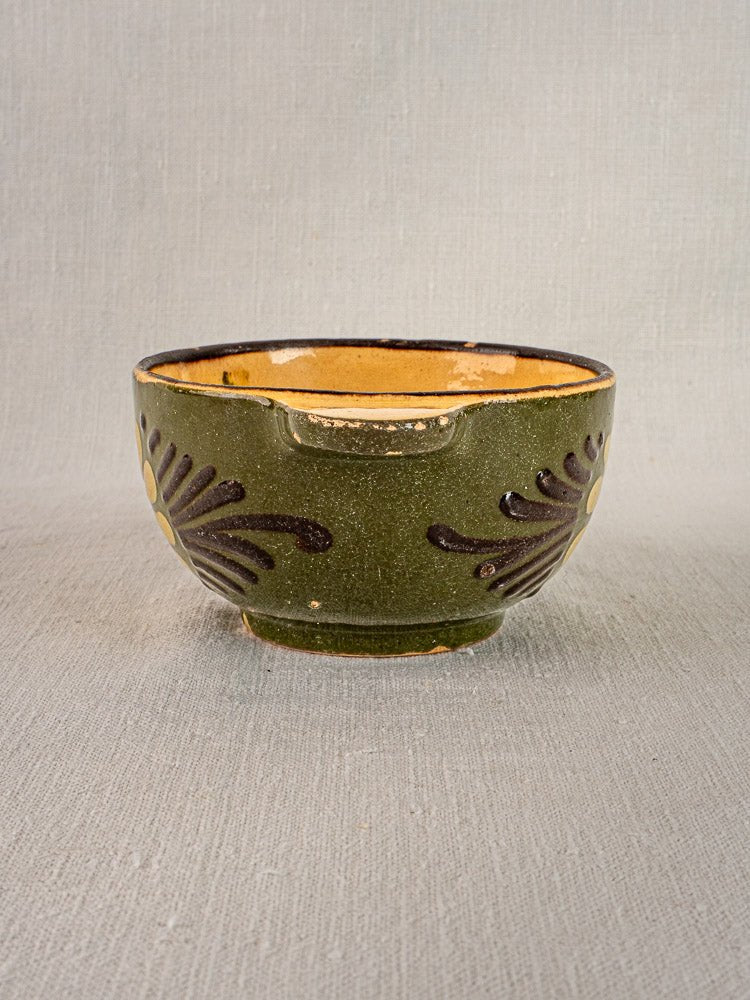 Savoyard green glazed French bowl with brown floral patterns and yellow interior on fabric background.