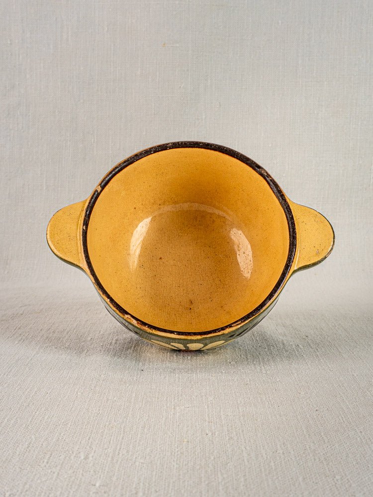 Green glazed ceramic handled bowl with rustic, vintage French style on light gray textured surface.