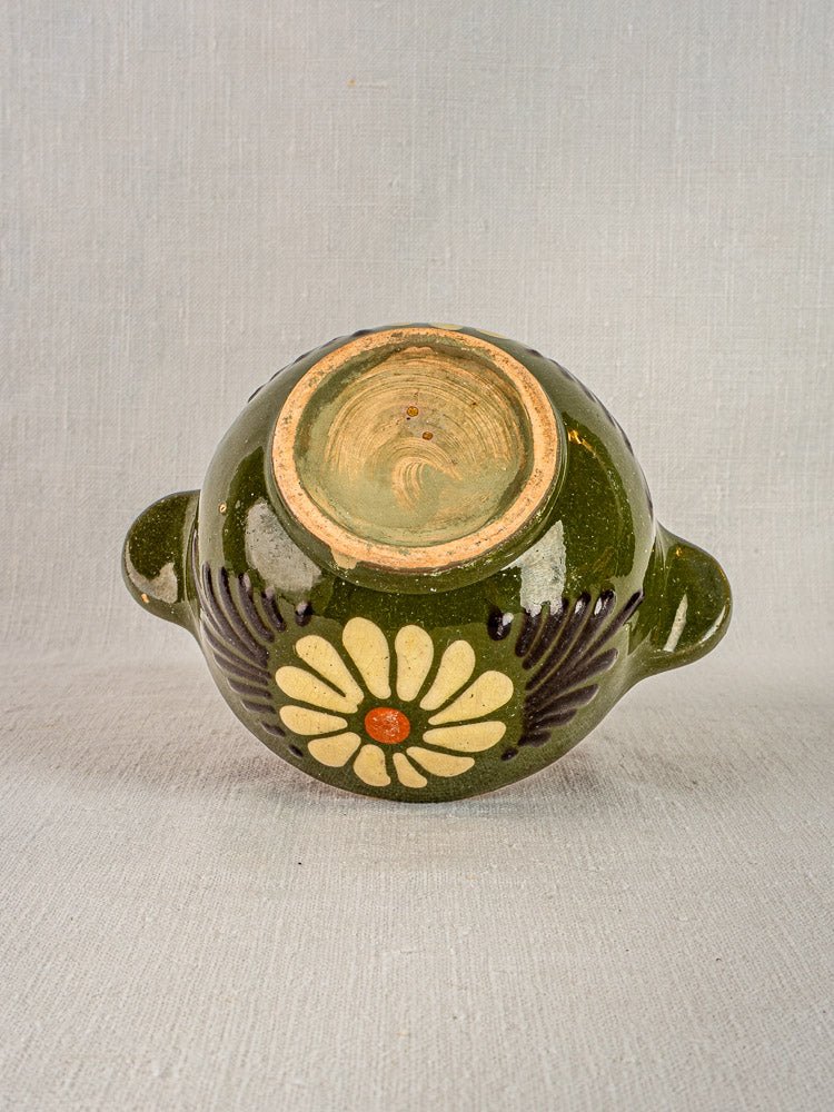 Green glazed French ceramic bowl with side handles, yellow floral motif, on light fabric background.