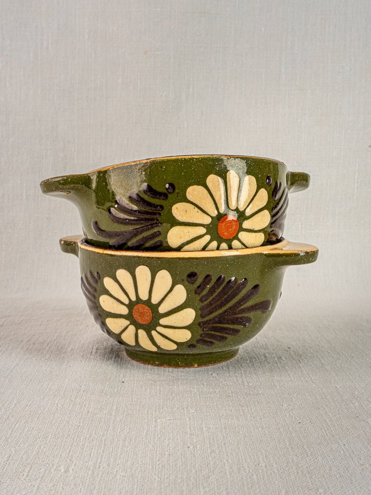 Pair of Savoyard green glazed vintage French pottery bowls with handles, daisy motif, stacked on light fabric.