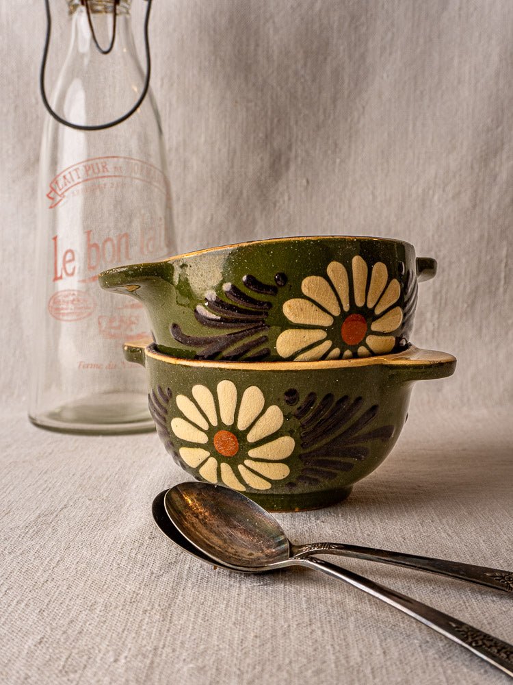 Vintage French green glazed bowls with handles and floral motifs, stacked on beige fabric.