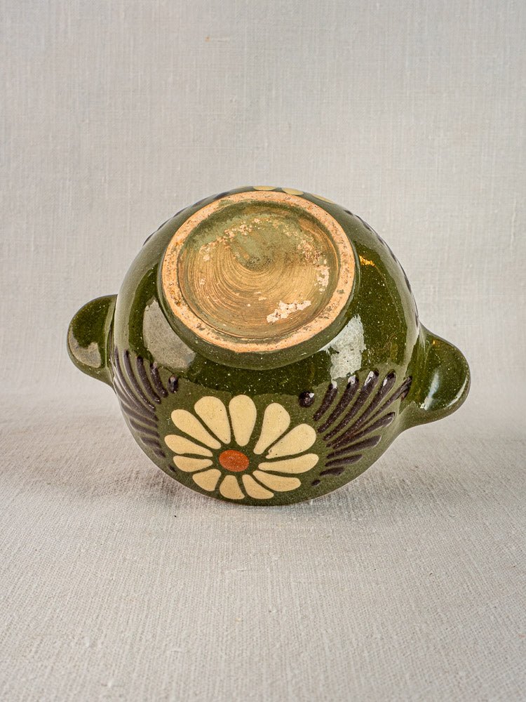 Savoyard green glazed vintage French bowl upside down, dual handles, floral motif, on neutral fabric.
