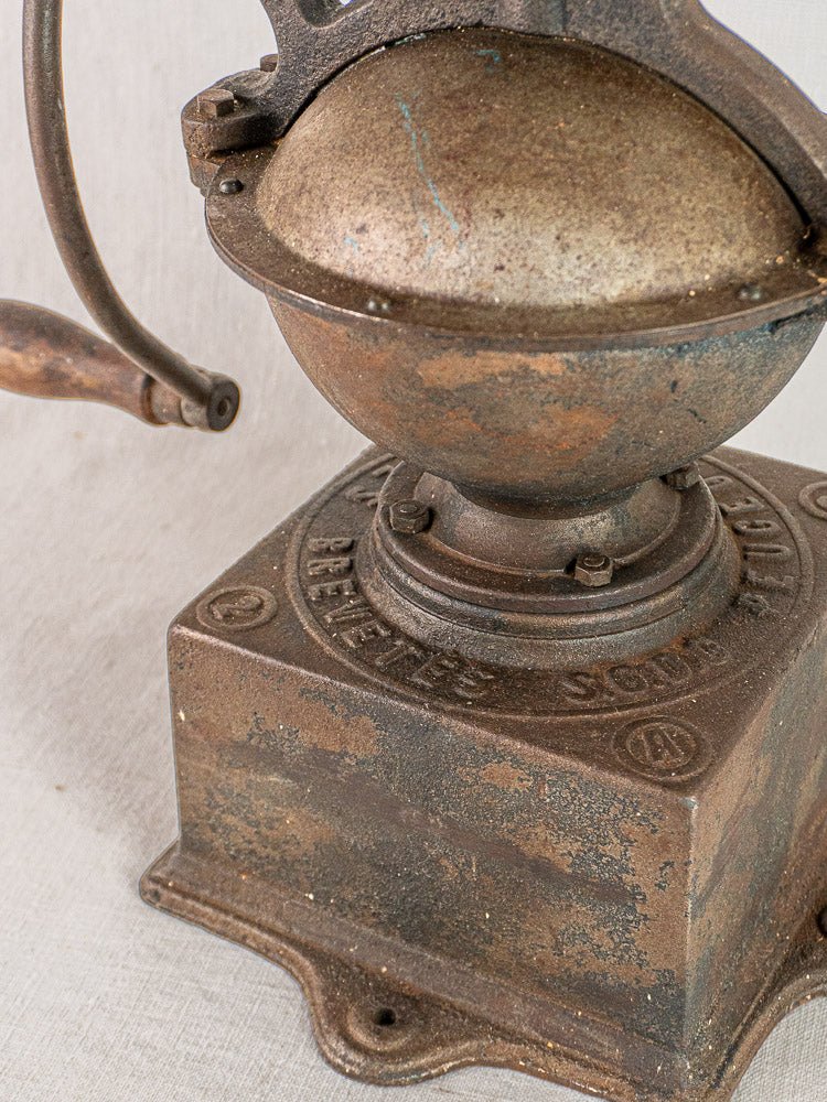 Antique French Peugeot Frères cast iron coffee mill with wooden handle and engraved base on light fabric.