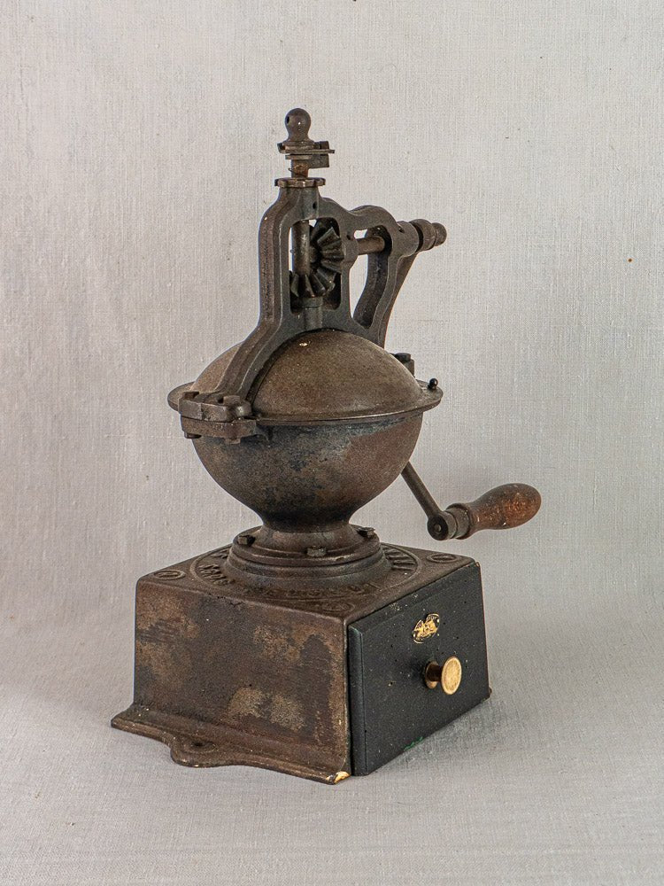 Antique French cast iron coffee mill by Peugeot Frères with wooden handle and drawer on light surface.