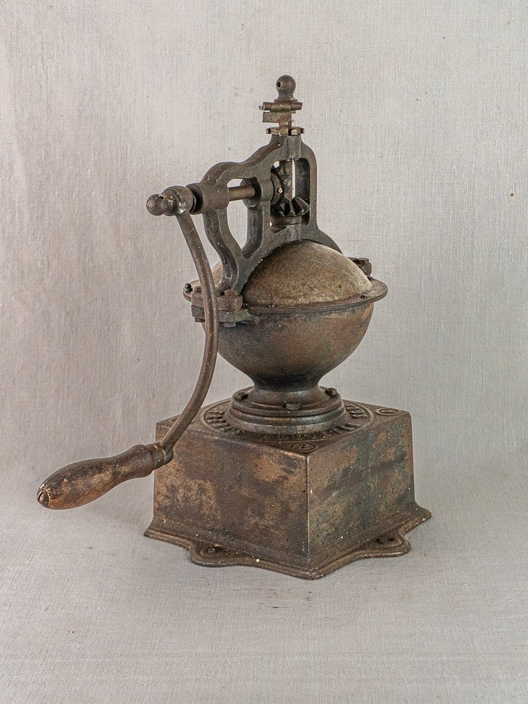 Antique French Peugeot Frères cast iron coffee mill with wooden handle on neutral fabric background.
