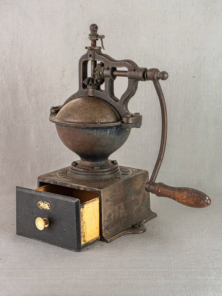 Antique French cast iron coffee mill by Peugeot Frères, classic handle and wood drawer, gray background.
