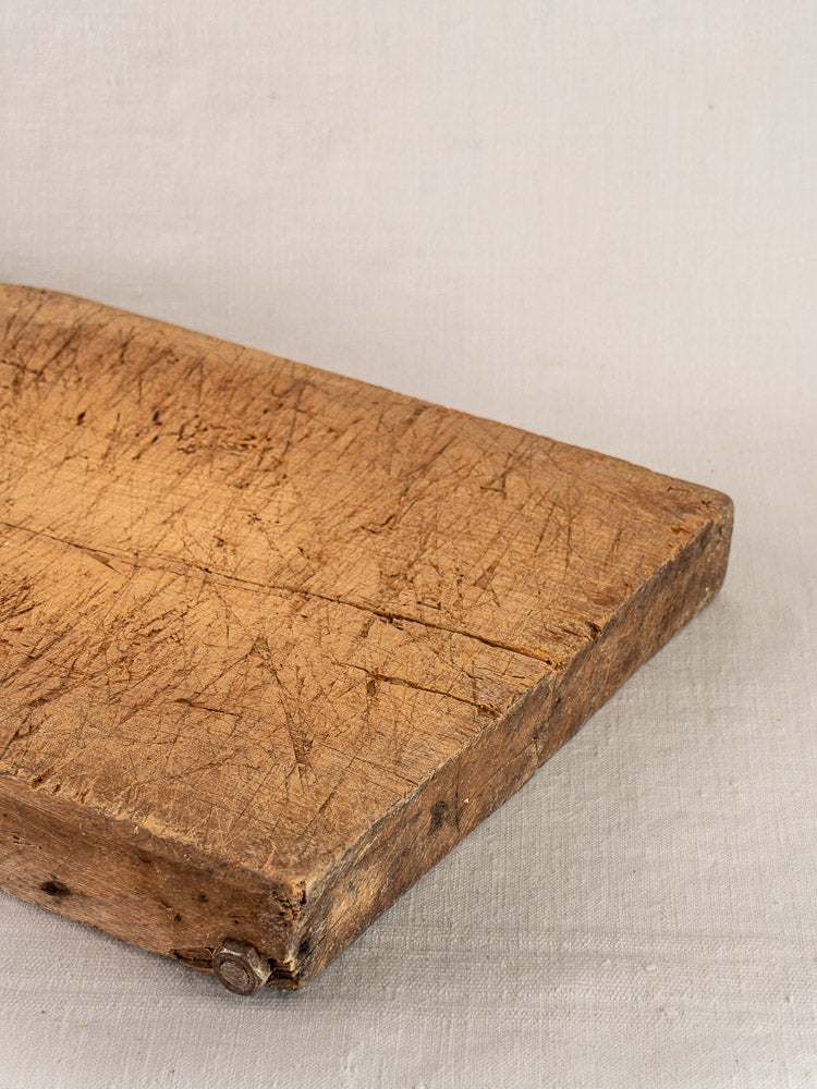 Antique French hand-carved cutting board with visible knife marks, early 19th century, on light fabric background.