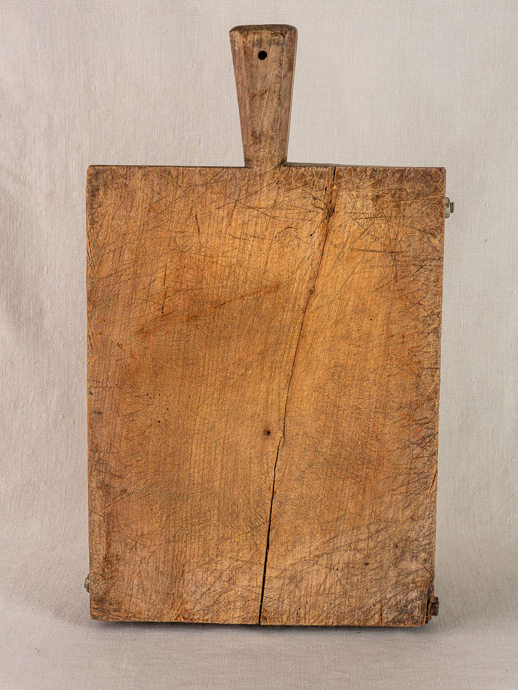 Antique French hand-carved cutting board, rectangular with a short handled top and crack, on light fabric.