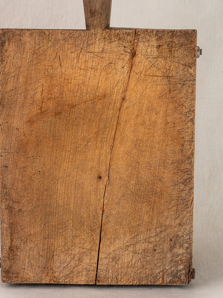 Antique French cutting board, early 19th century, hand-carved with worn wood, scratches, a crack, and partial handle.
