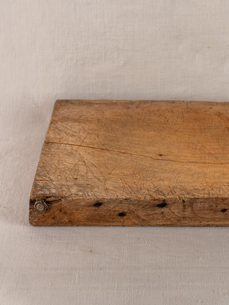 Antique French hand-carved cutting board with visible age marks, early 19th century, on neutral fabric.