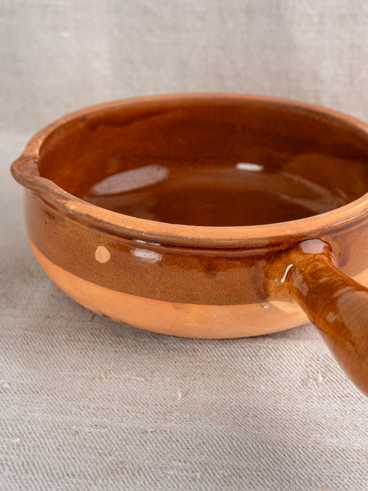 Antique French terracotta poêlon with glazed interior and rim, unglazed lower exterior, on textured fabric.