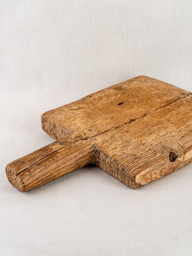 Antique French primitive cutting board, 18th century, rustic and weathered, on light fabric background.