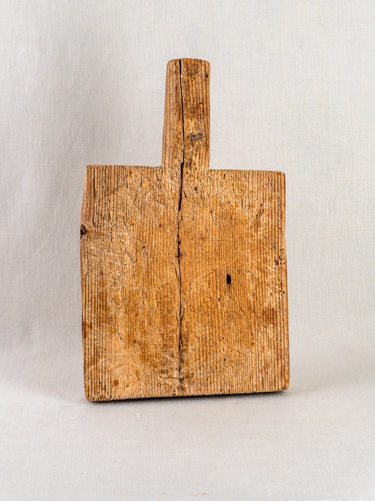 Antique 18th-century French cutting board with handle, visible wood grain, wear, and age cracks.