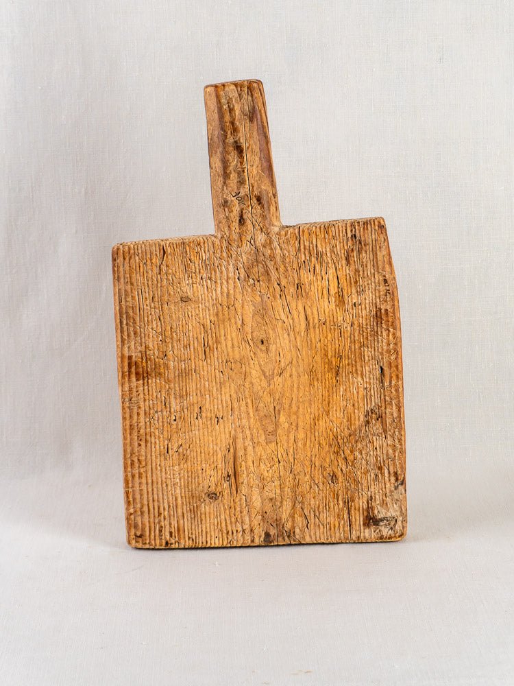 Antique French primitive cutting board, 18th century, with worn wood and rich patina, upright on a pale background.