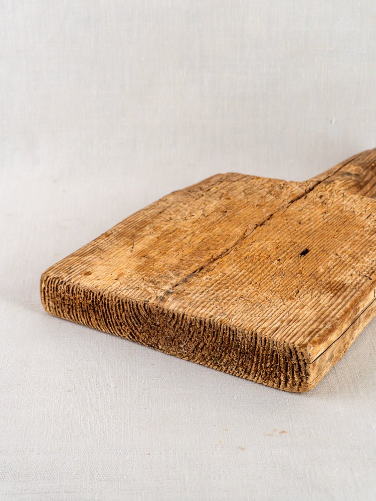 French 18th-century primitive cutting board with visible grooves and aged, textured wood against a light background.