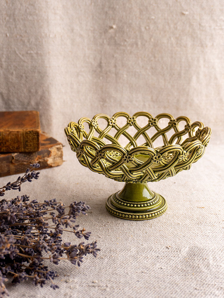 Antique French Pichon Uzès olive green compote with openwork on beige cloth beside dried lavender and vintage books.