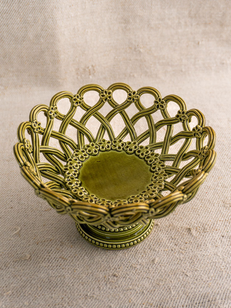 Antique French Pichon Uzès compote in olive green with openwork lattice, on textured beige fabric background.
