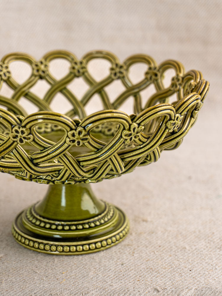 Antique French Pichon Uzès compote in olive green with openwork pedestal basket, on beige textured fabric backdrop.