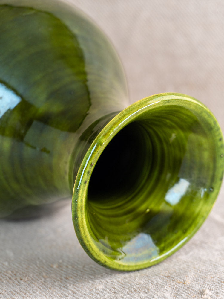 Vintage French Pichon Uzès green glazed earthenware vase, mid-20th century, displayed on a textured beige surface.